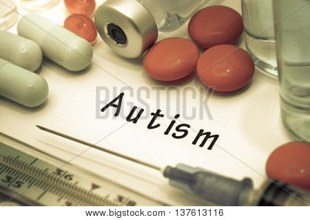 autism - diagnosis written on a white piece of paper. Syringe and vaccine with drugs.