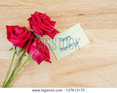 Three red rose flower and handwriting Happy Monday on notepaper with wood background in top view