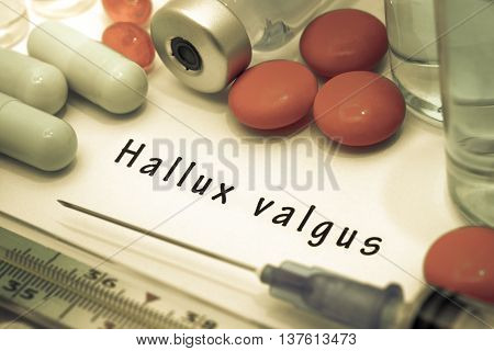 Hallux valgus - diagnosis written on a white piece of paper. Syringe and vaccine with drugs.
