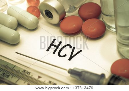 HCV - diagnosis written on a white piece of paper. Syringe and vaccine with drugs.