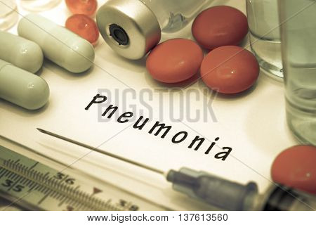 Pneumonia - diagnosis written on a white piece of paper. Syringe and vaccine with drugs