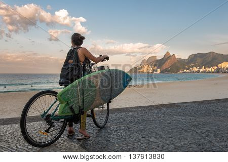 Rio de Janeiro, Brazil - July 7, 2016: Female surfer on a bike looking at the ocean in Ipanema beach.