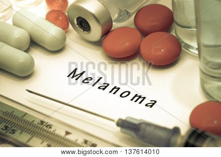 Melanoma - diagnosis written on a white piece of paper. Syringe and vaccine with drugs.