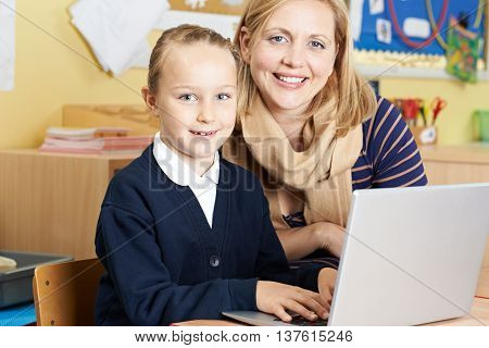 Teacher Helping Female Elementary School Pupil In Computer Class