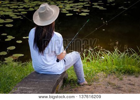 Young woman fishing in pond in summer evening