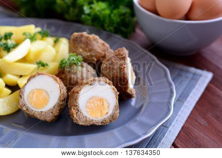 Scotch eggs with boiled potatoes on a gray plate