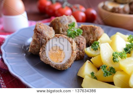 Scotch eggs with boiled potatoes on a gray plate