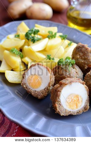 Scotch eggs with boiled potatoes on a gray plate
