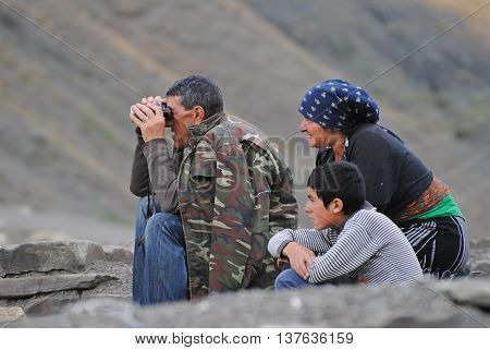 Xinaliq, Azerbaijan - August 23, 2014. Shepherd family in Xinaliq mountainous village. A man looking into binoculars, with woman and child by his side.