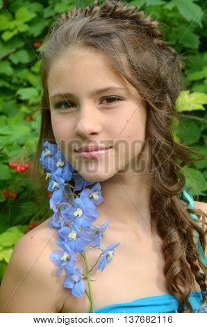 Young girl with a fine weave and long hair in the garden near blooming delphinium