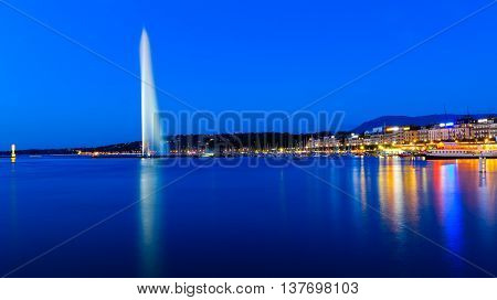 The famous national landmark Jet d'eau as seen from Jardin Anglais on a summer night. To the right is the Eaux-vives waterfront