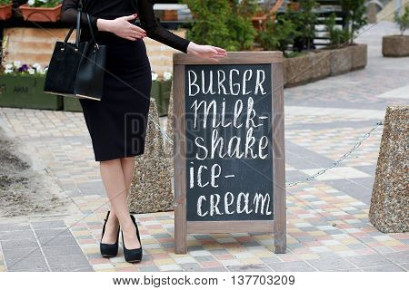 Elegant woman points hand on the chalk stand advertising street cafe. Wooden blank for text