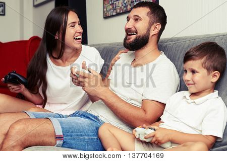 Young happy family is rapt in playing a videogame together using joysticks at home 