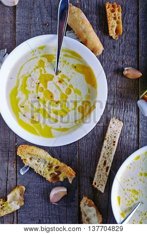 Homemade garlic cream soup with toasted ciabatta on dark and old wood background