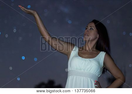 Young woman holding blurred  Star. Woman under starry night. Woman in white long dress looking to starry night. Blurred night sky Selective focus shallow depth of field