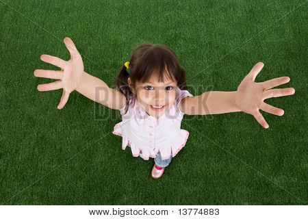 Por encima de la vista del niño feliz sobre la hierba verde y levantando sus brazos a la cámara