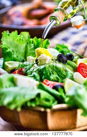 Vegetable lettuce salad. Olive oil pouring into bowl of salad. Italian Mediterranean or Greek cuisine. Vegetarian vegan food.