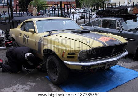 PERM RUSSIA - JUNE 29 2016: Rally of retro-cars Peking-Paris 2016 June 29 2016 in Perm Russia. Member of the rally repairing the car Ford Mustang.