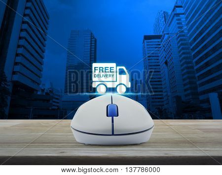 Wireless computer mouse with free delivery truck icon on wooden table in front of city tower background Transportation business concept