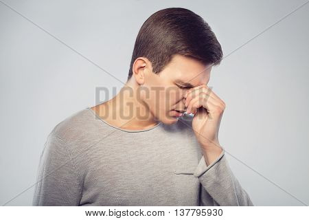 Feeling sick and tired. Frustrated young man massaging his nose and keeping eyes closed isolated on gray background