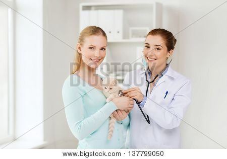 medicine, pet, animals, health care and people concept - happy woman and veterinarian doctor with stethoscope checking scottish fold kitten up at vet clinic