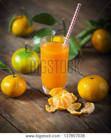 Glass of fresh tangerine juice with ripe tangerines leaves and old-fashioned straw