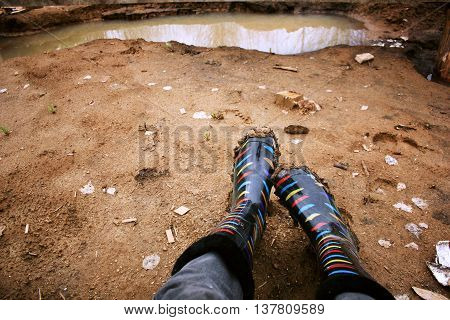 Legs in colored rubber boots soiled with clay amid puddles.