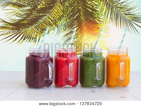 Smoothy drinks in glass jars on white table under plam tree