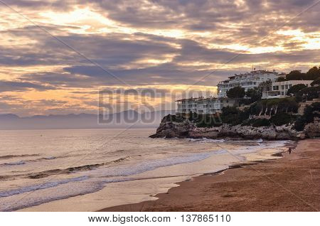 Deserted beach at sunset beautiful cloudscape resort on rock man running along the shore. Salou Spain. Summer vacations concept. Horizontal.