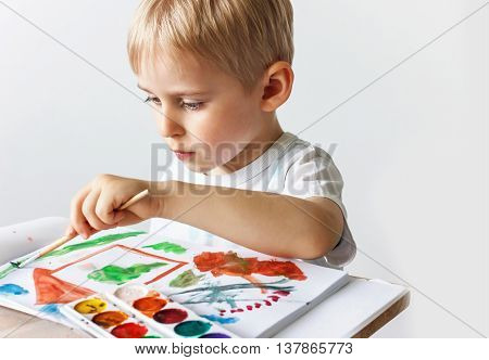 Happy Cheerful Child Draws Paints In An Album, Using A Variety Of Drawing Tools. Creativity Concept