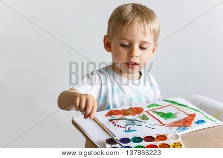 Happy Cheerful Child Draws Paints A Southpaw In The Album, Using A Variety Of Drawing Tools. Creativ