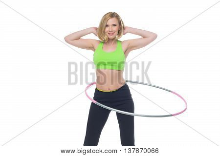 Beautiful middle aged blond fit woman in green bra top and black pants doing sport exercise with hula hoop. Isolated over white background. Copy space.