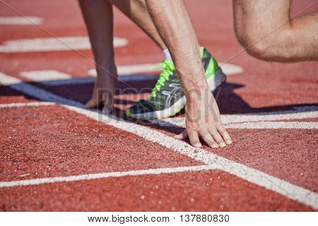 low start. Sprinter legs and hands on line of rubber stadium running path
