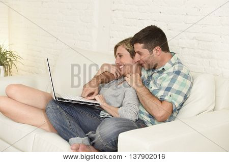 young attractive 30s couple in love sitting on couch together with laptop computer happy at home living room using the internet smiling cheerful and satisfied in technology and lifestyle concept