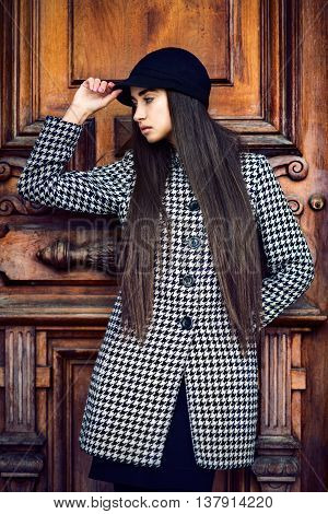 Beautiful fashionable brunette woman with long hair posing near wooden door wearing coat and a hat