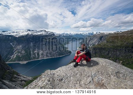 The summer view of man sitting on the rock next to the Trolltunga cliff (The Troll's tongue) in Odda