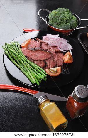 business lunch fresh roast beef meat slices on black plate wotj cutlery asparagus boiled broccoli rye bun on wooden table