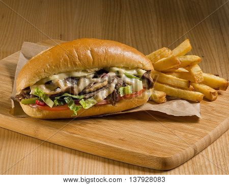 cheesesteak sandwich on cutting board with fries