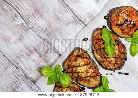 Baked eggplant stuffed with vegetables and cheese with addition aromatic herbs and sauce on paper. Delicious vegetarian dish. top view, sopy space