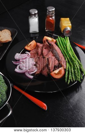 business lunch fresh roast beef meat slices on black plate wotj cutlery asparagus boiled broccoli rye bun on wooden table