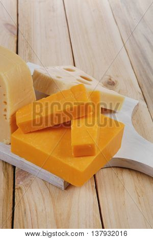 various types of fresh raw aged delicatessen cheese on white plate over light wooden table cheddar edam swiss