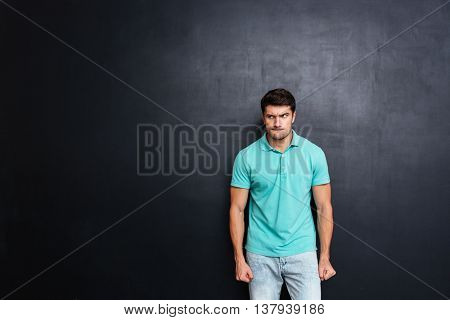 Angry irritated young man stnding and looking away over chalkboard background
