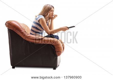 Young woman watching TV and biting her nails seated on an armchair isolated on white background