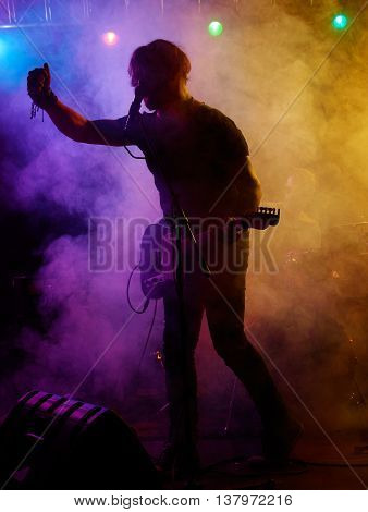 Silhouette of guitar player on stage. Dark background, smoke, spotlights