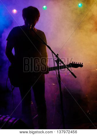 Silhouette of guitar player on stage. Dark background, smoke, spotlights