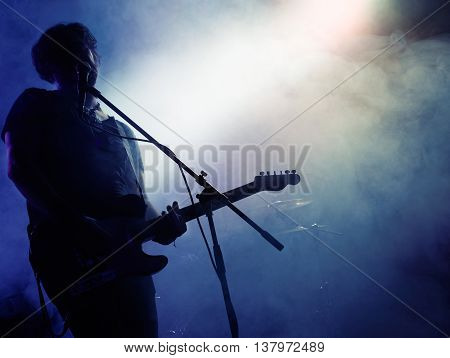 Silhouette of guitar player on stage. Dark background, smoke, spotlights