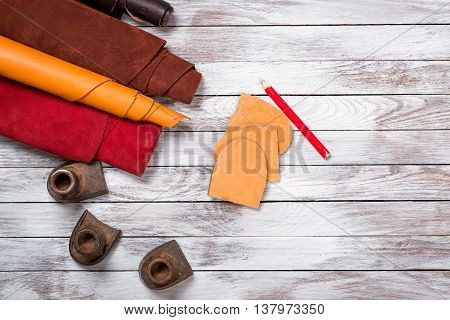 Brightly colored leather in rolls working tools shoe lasts notebook with pencil on white wooden background. Leather craft.