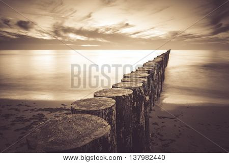Coast with piles during sunset long exposure blurring water.Vintage photo of baltic Poland.