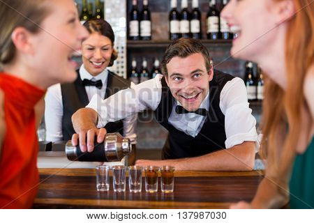 Bartender pouring tequila into shot glasses at bar counter in bar