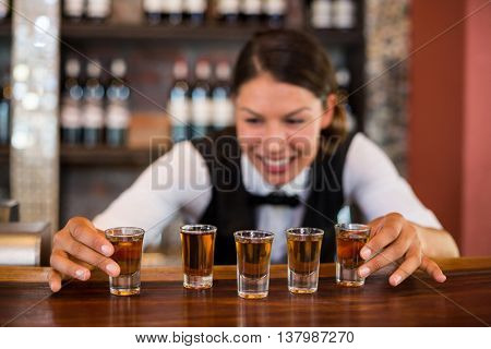 Bartender placing shot glasses in a row on bar counter in bar